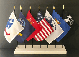 seven miniature US military flags in a white rectangular flag stand