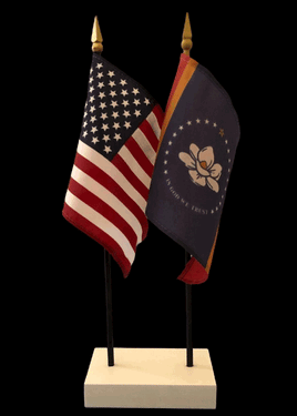 a photo of two miniature flags set in a white square base: the left flag is the american flag, and the right flag is a state flag